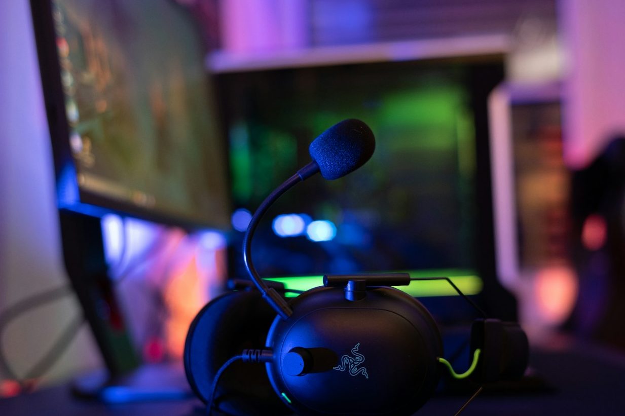 Shows a headphone laying on a desk in front of a gaming pc