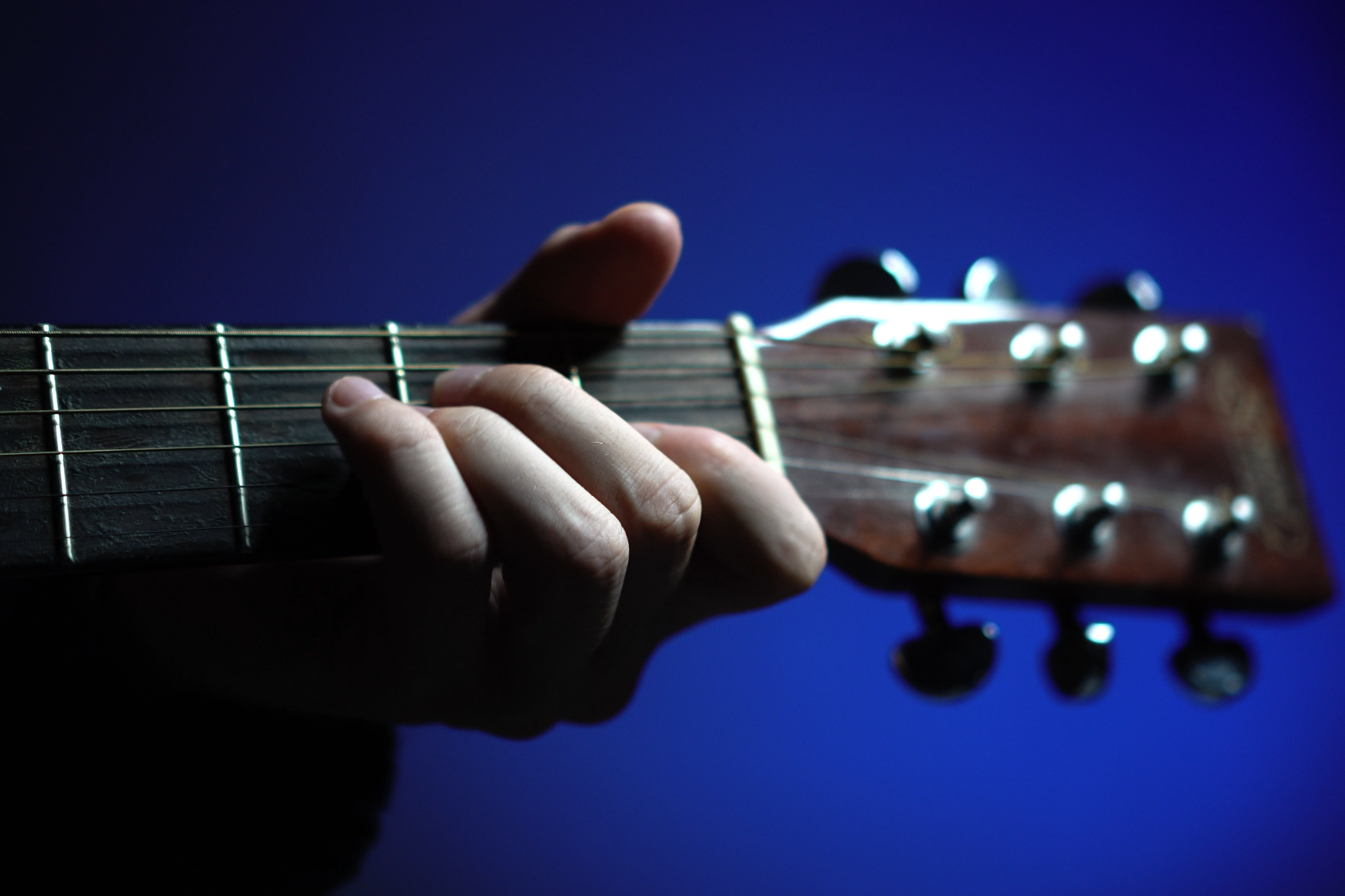 A close up of a guitarneck with hands gripping a chord